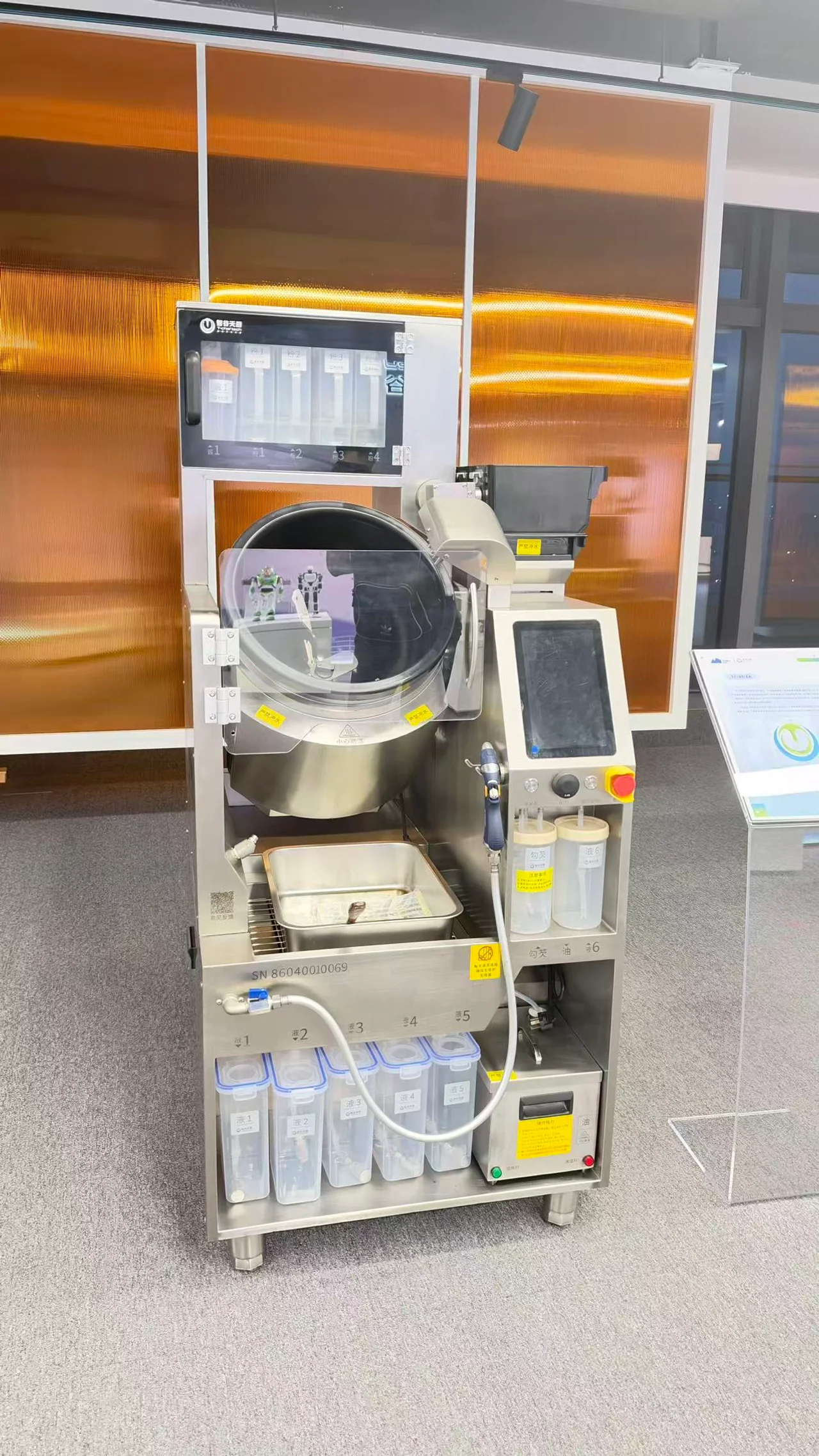 Automated cooking robot with a stainless-steel wok, ingredient dispensers, and touchscreen controls.