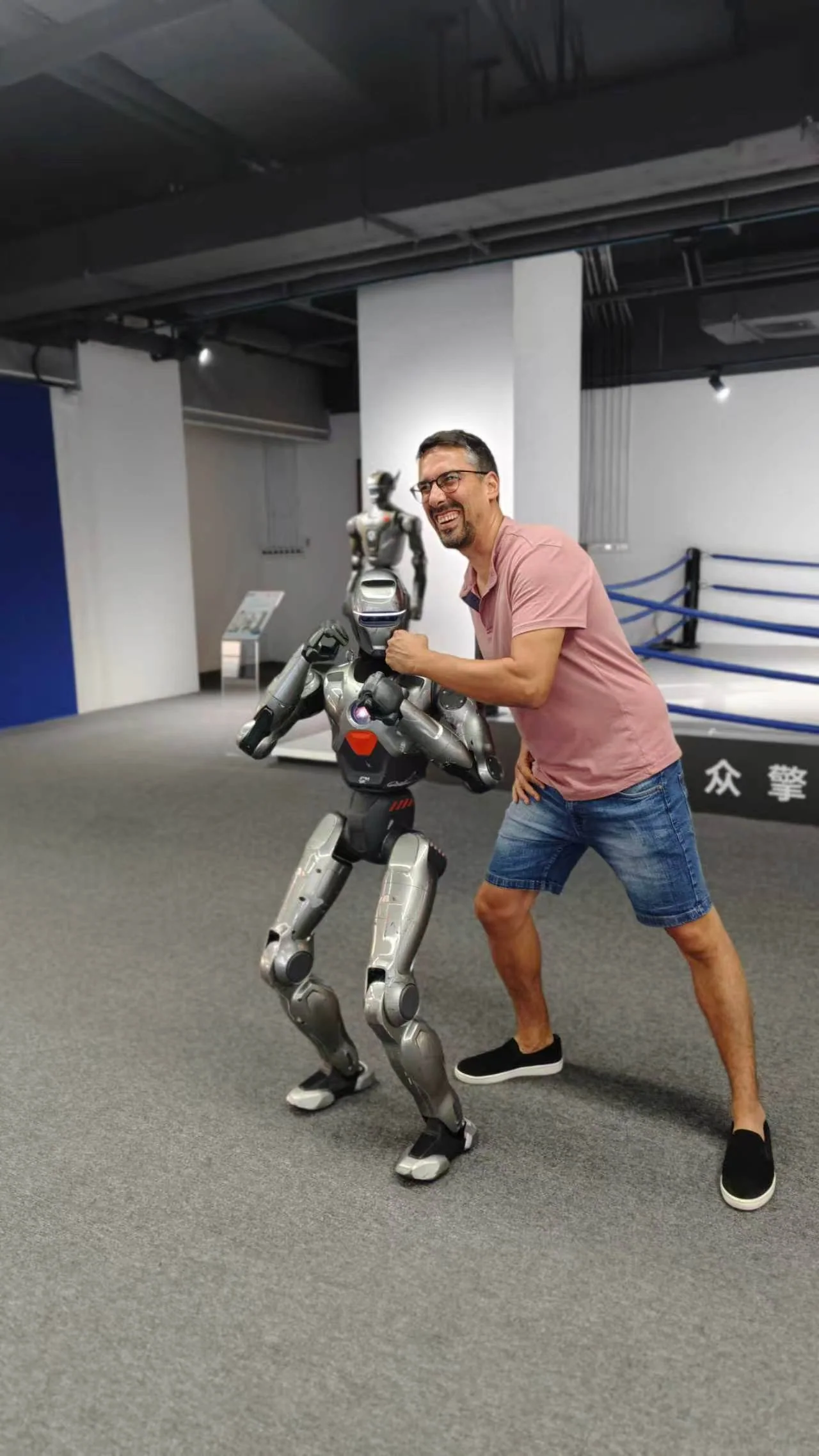 A visitor posing beside a compact silver humanoid robot.